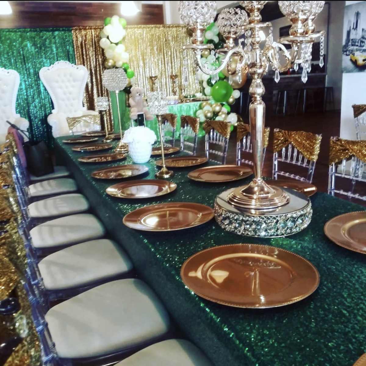 A long dining table set with golden plates and decorated with green and gold accents in a festive setting.