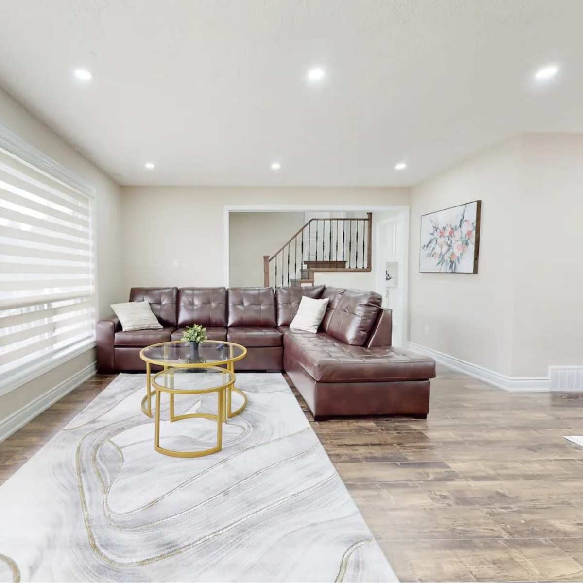 A modern living room with a brown sectional sofa, a round coffee table, and large windows featuring sheer blinds.
