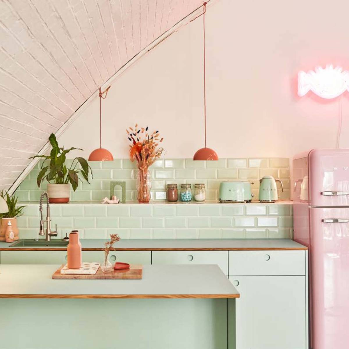 A modern kitchen featuring pastel green cabinets, a pink refrigerator, and decorative items on the counter and shelves.