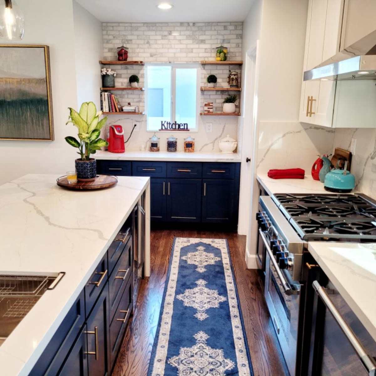 A modern kitchen featuring a central island with a sink, dark cabinetry, and a stove, complemented by a rug running across the wooden floor.