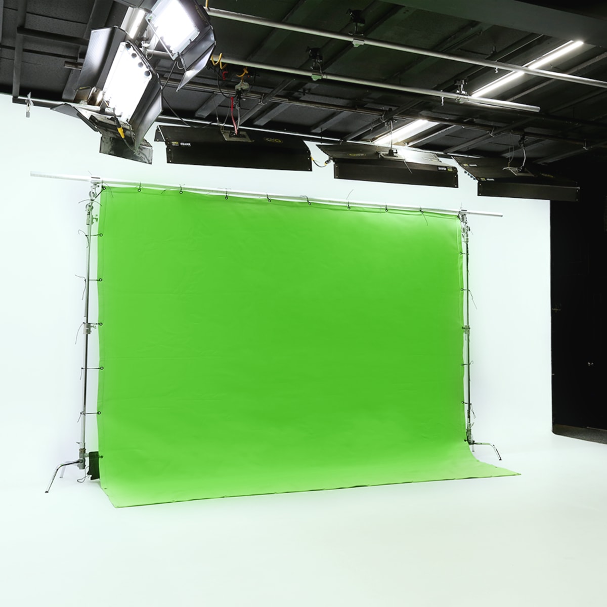 A photography studio with a green backdrop, bright lighting fixtures above, and equipment stands arranged on the side.
