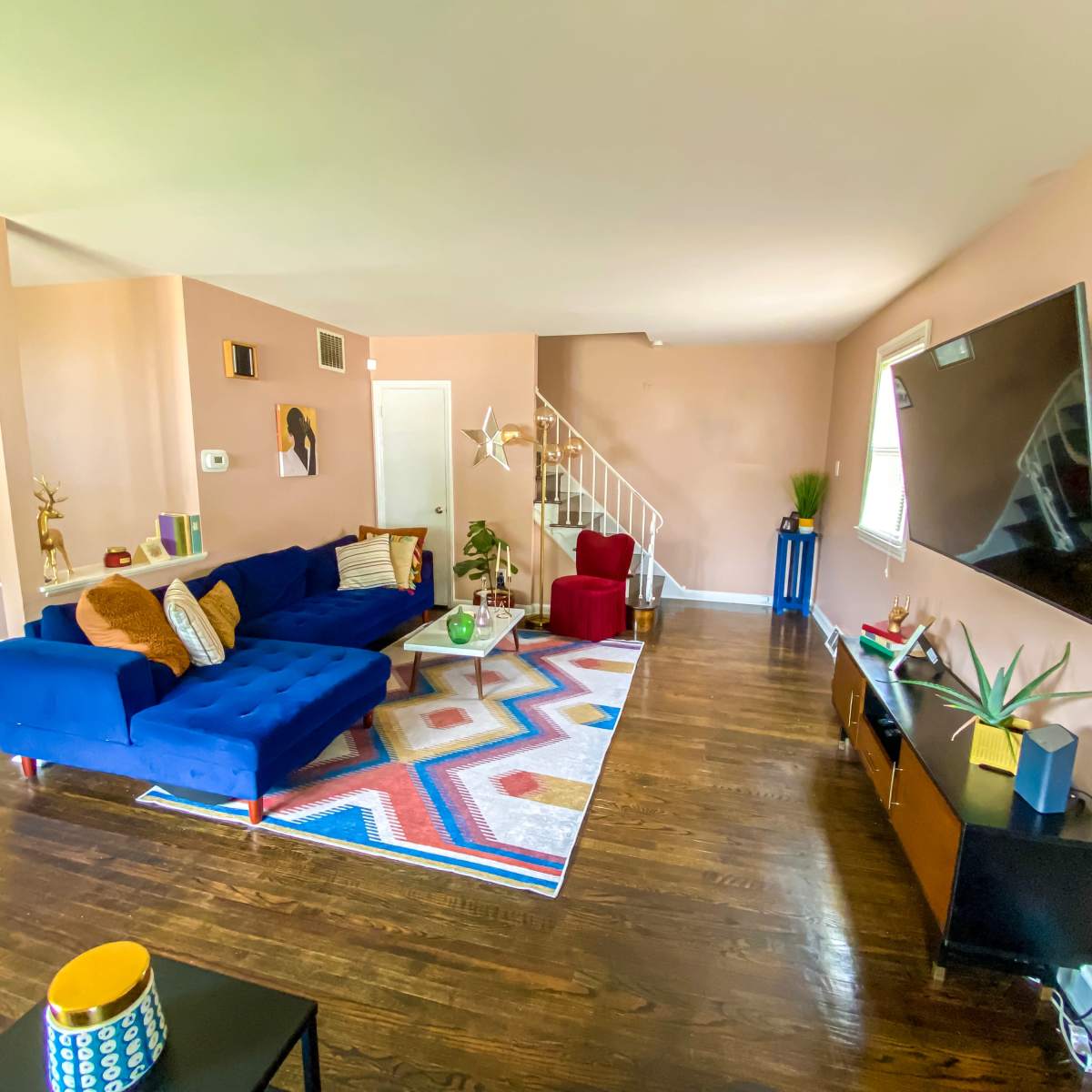 The living room features a blue sectional sofa, a colorful area rug, and a large wall-mounted television.