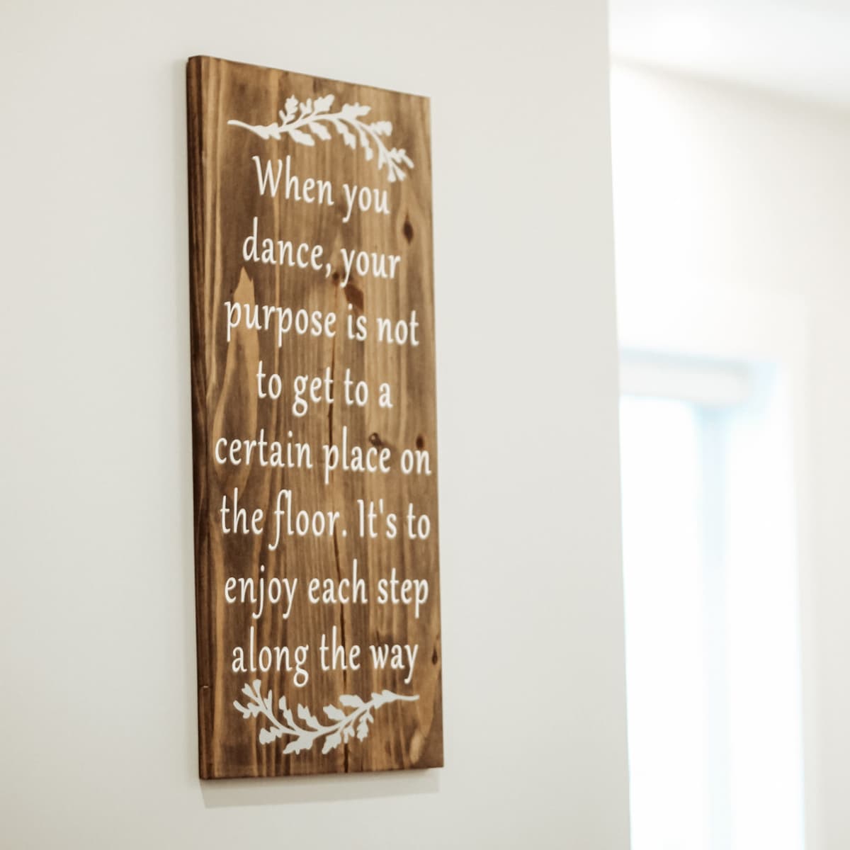 A wooden sign with white lettering on a wall conveys a message about the purpose of dancing.