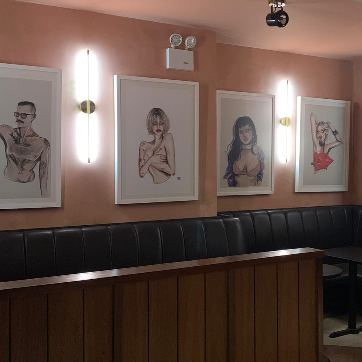 A corner of a restaurant with framed artistic illustrations on the walls and a dark booth seating area.