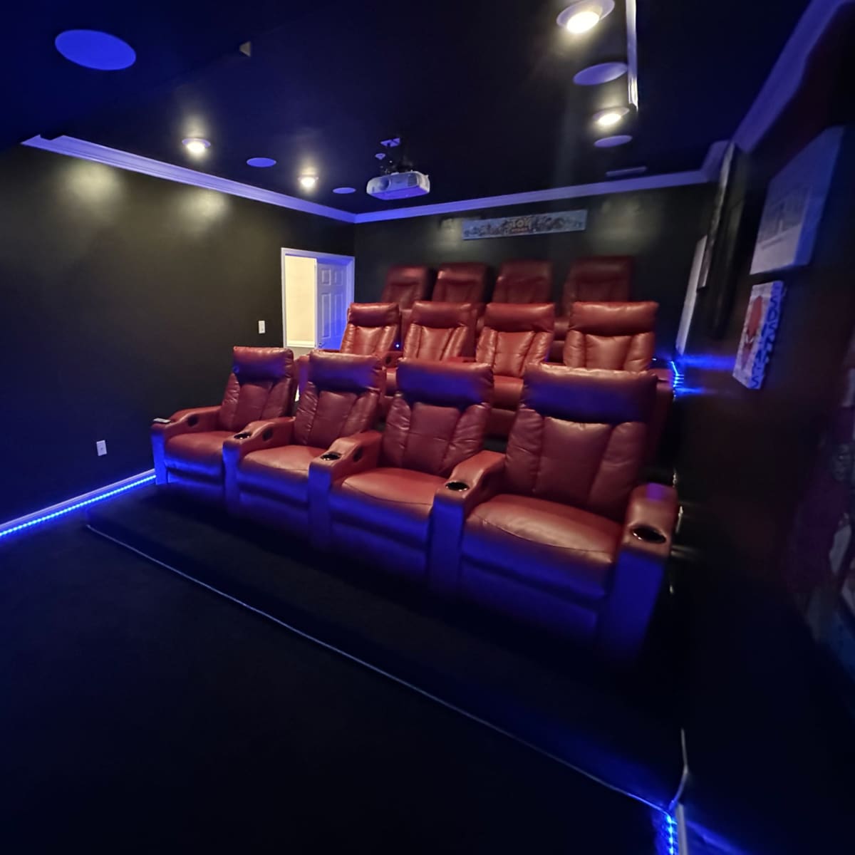 An intimate home theater with seven red reclining seats arranged in a dark room, illuminated by blue LED lighting along the floor.