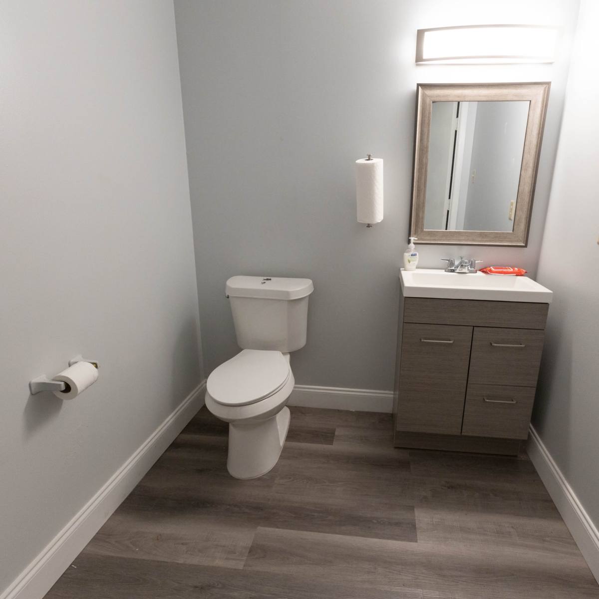 A small bathroom with a toilet, a sink with a mirror above it, and light gray walls.