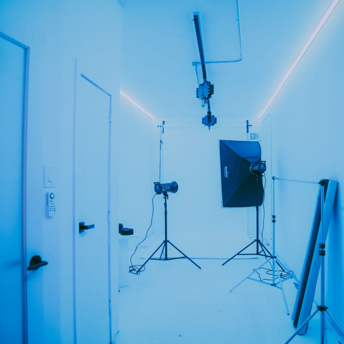 A well-lit studio room with blue walls, featuring backdrop supports, lighting equipment, and two doors.