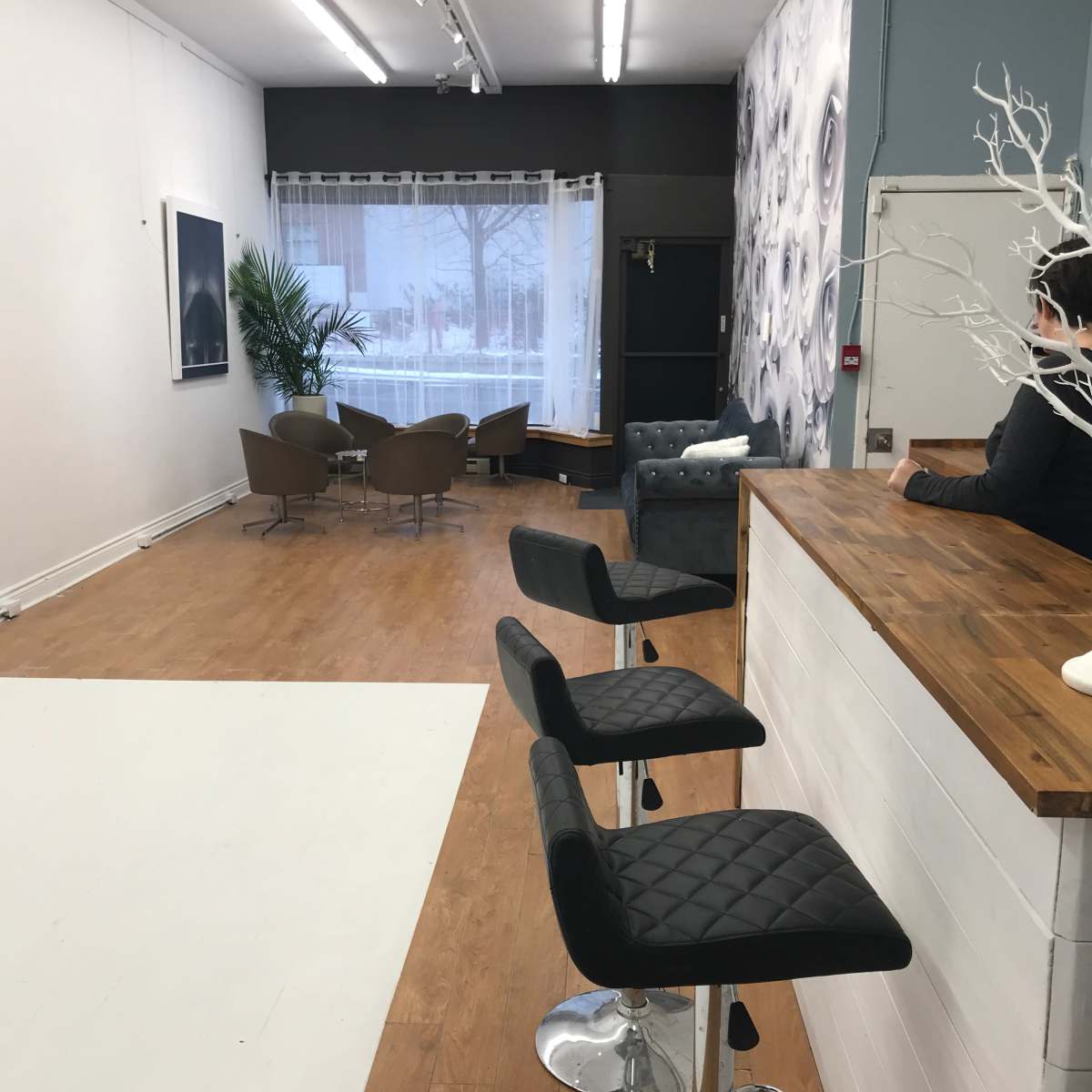 A modern interior space featuring a bar with stools on one side and a seating area with chairs and a large window on the opposite side.