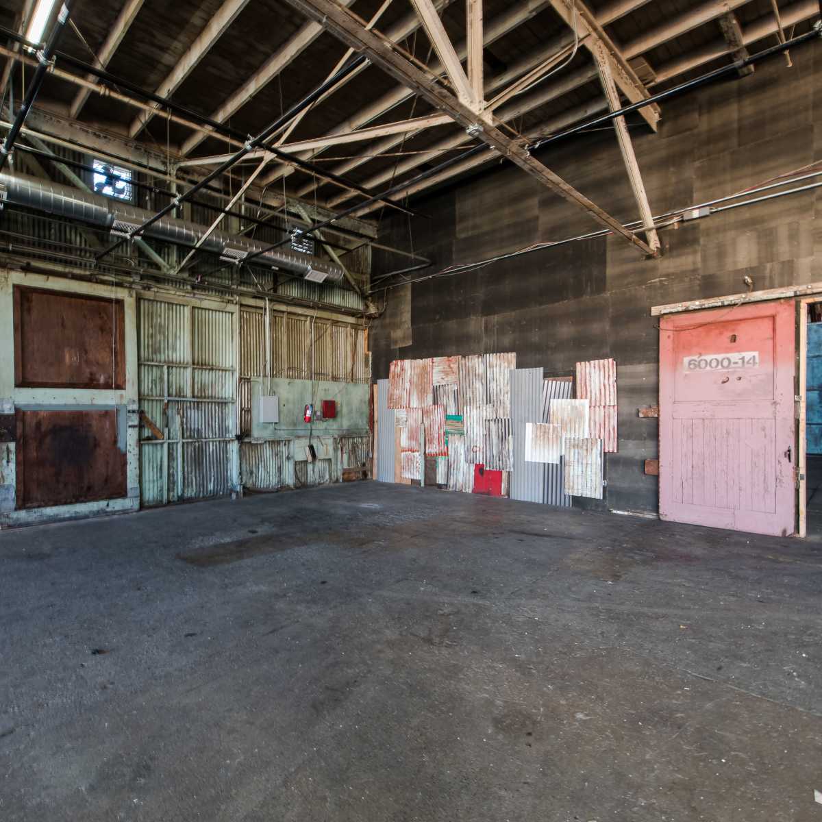 An industrial space with weathered walls, multiple large doors, and a colorful display of arranged panels on one side.