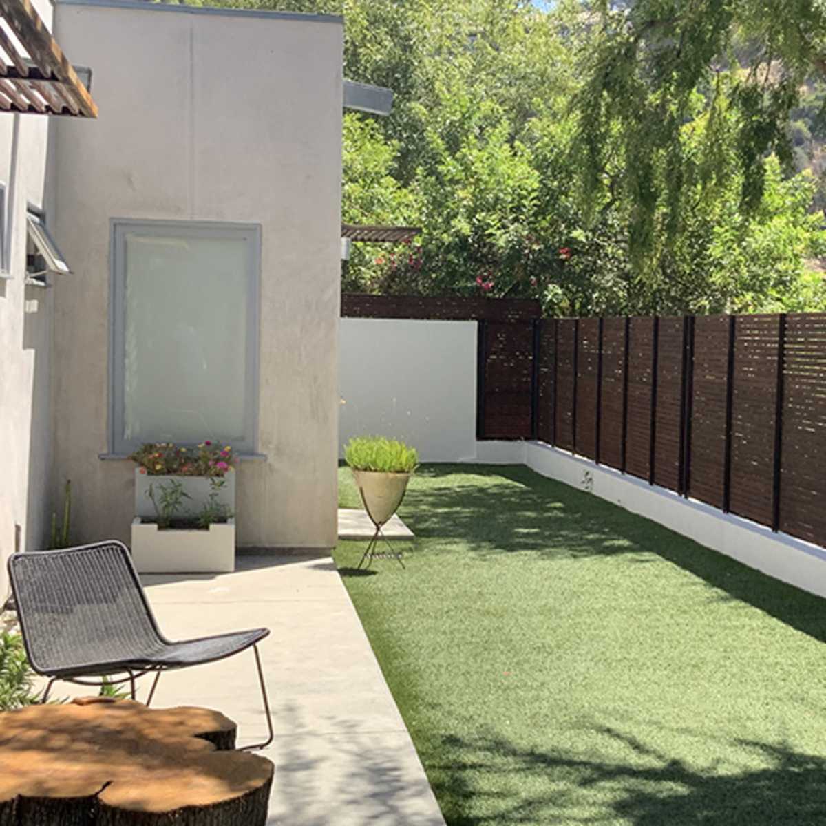 A modern backyard with artificial grass, a wooden privacy fence, a garden area with a planter, and a chair positioned on a concrete patio.
