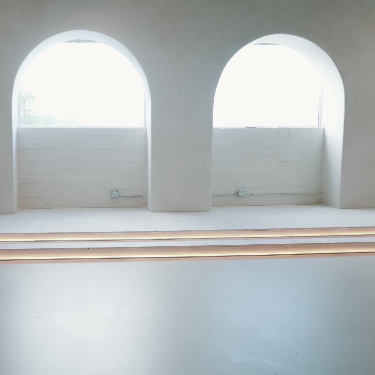 A minimalist interior space with two large arched windows and three steps leading up to a raised platform.