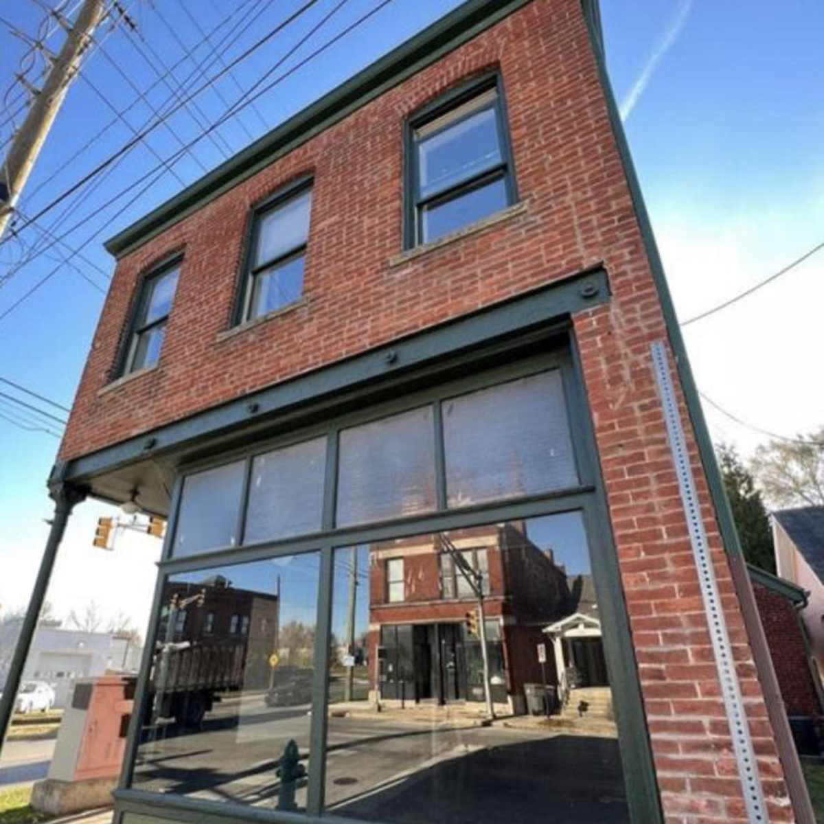 A brick building with large glass windows at a street corner, featuring a green trim and a clear blue sky above.