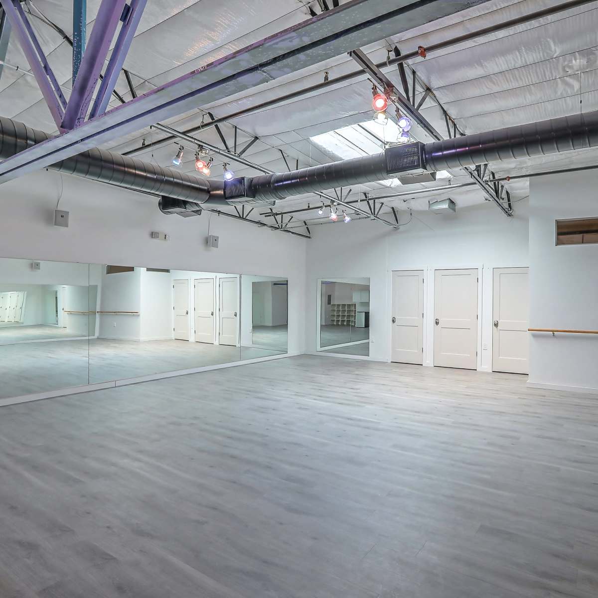 A spacious, empty dance studio with mirrored walls, wooden flooring, and overhead lighting.