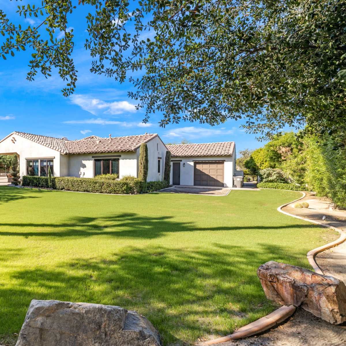 A single-story house with a tiled roof surrounded by a well-maintained lawn and landscaping.