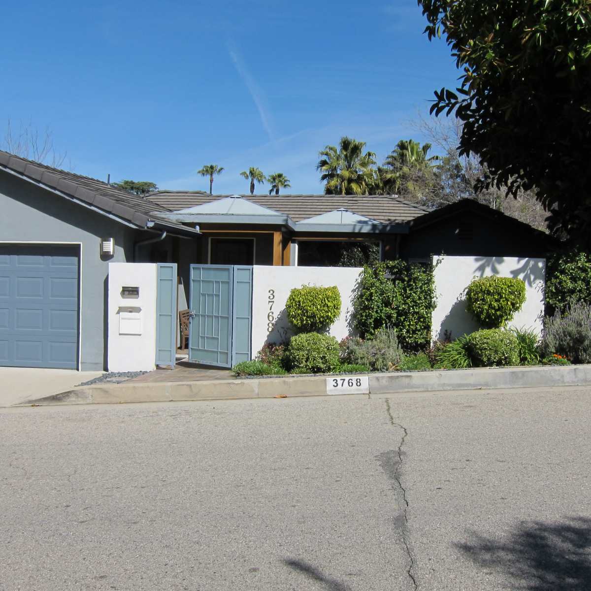 A single-story house with a gray garage door, a decorative front gate, and neatly trimmed landscaping along the sidewalk.