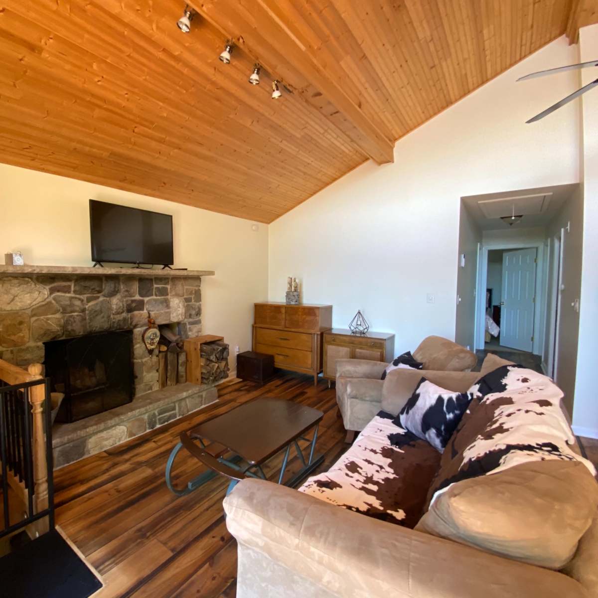 A living room with a stone fireplace, wooden ceiling, and a sofa facing a coffee table.