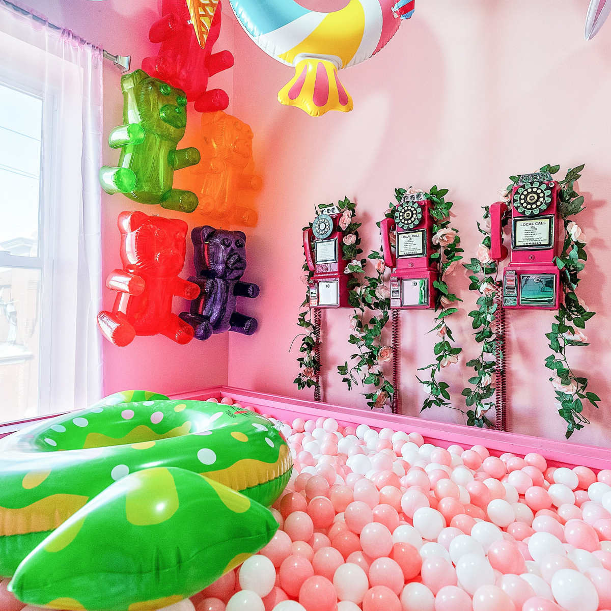 The scene features a brightly colored room with a pink ball pit, adorned with large gummy bear decorations and framed awards on the walls.