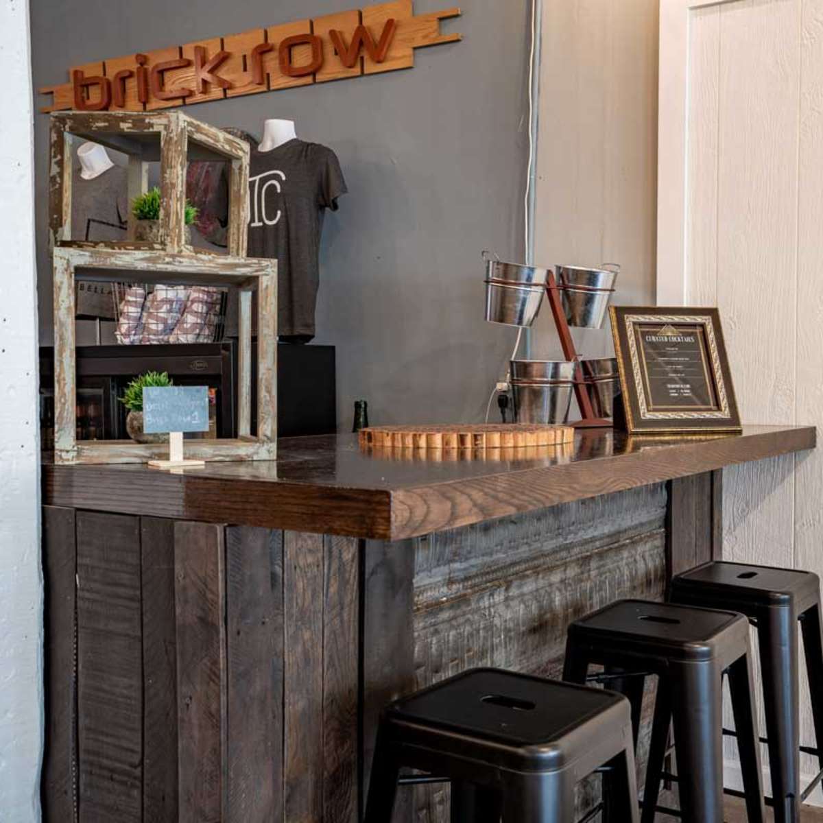 A rustic wooden bar with metal stools, featuring a display of merchandise and a framed certificate on a counter.