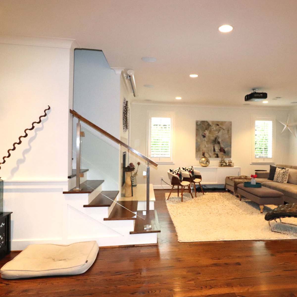 The living room features a sectioned layout with a staircase, modern furniture, and large windows allowing natural light to fill the space.