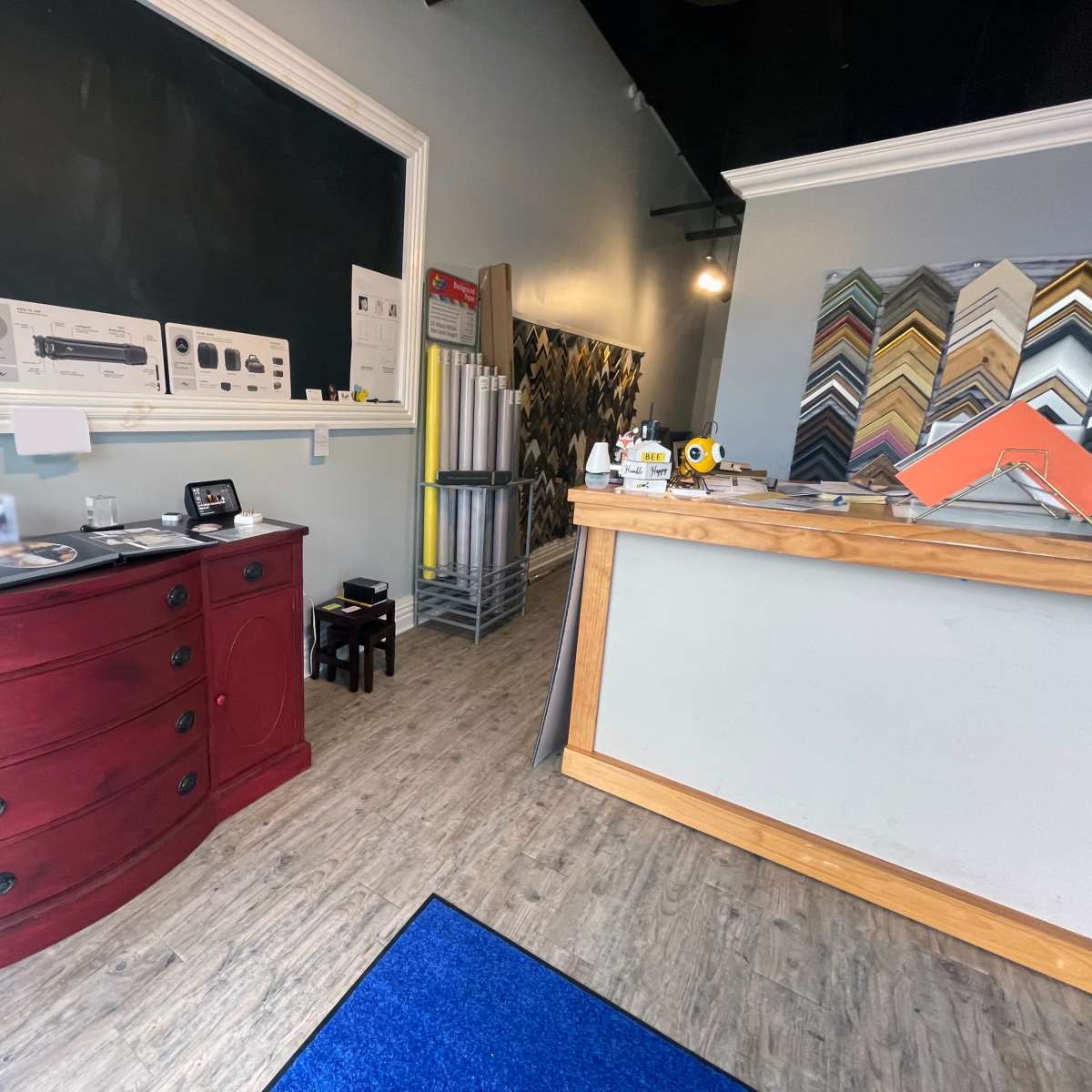 The interior of a frame shop featuring a red display cabinet, a service counter, and various framing supplies on a wall.