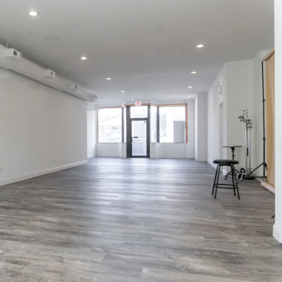 A large, empty room with wooden floors and a wide entrance door leading to the outside.