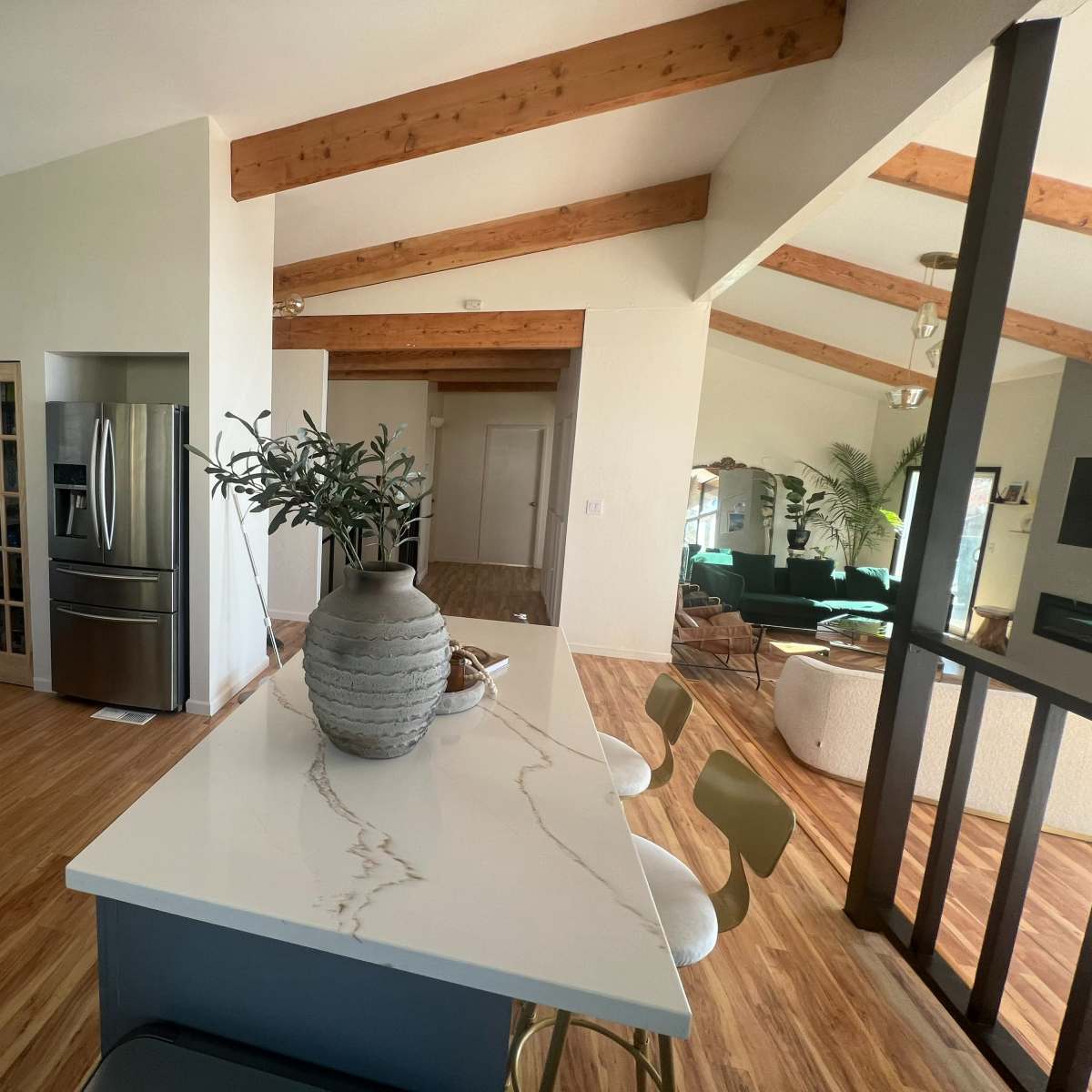 A modern kitchen features blue cabinetry and a marble countertop, leading into a living area with high ceilings and a mixture of furniture.