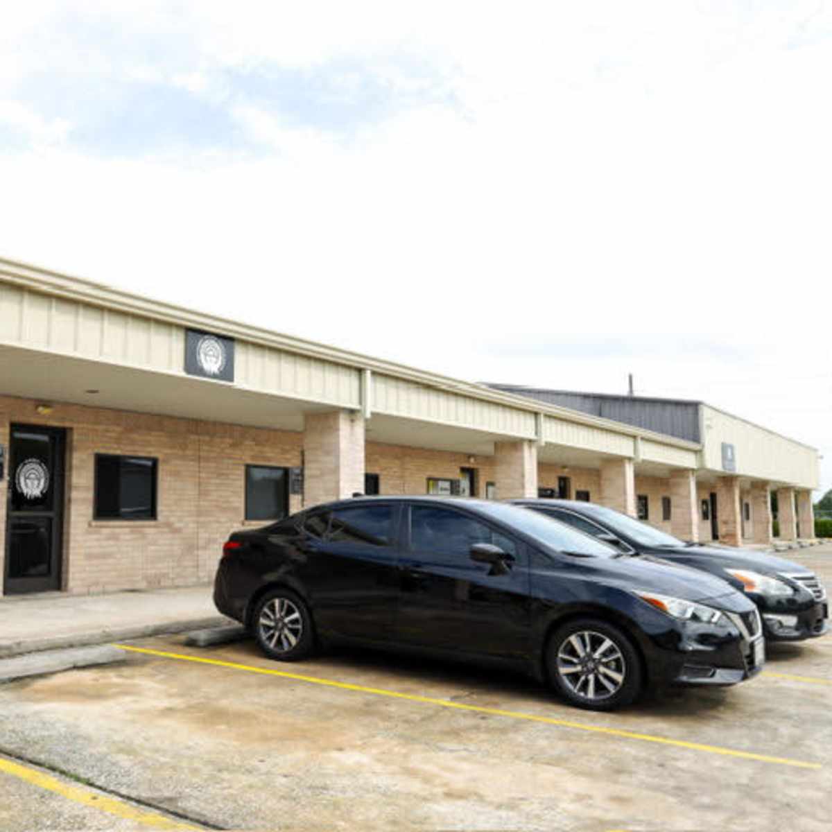 A row of commercial buildings with a parking lot containing two black cars.