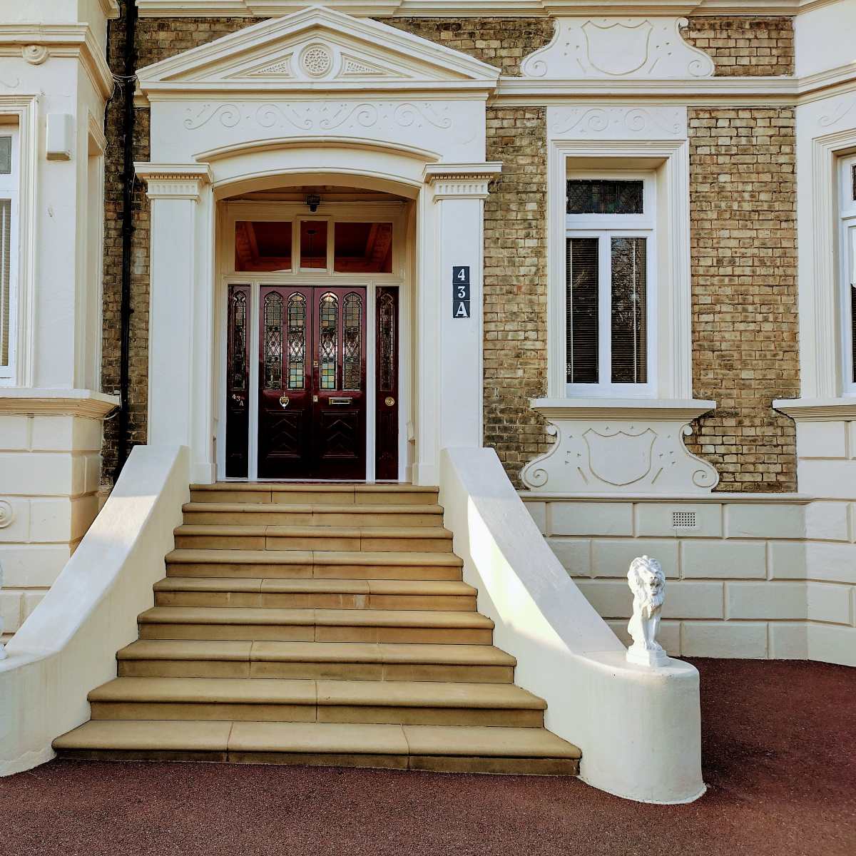 A building entrance with a set of steps leading up to double wooden doors, flanked by stone lion statues.