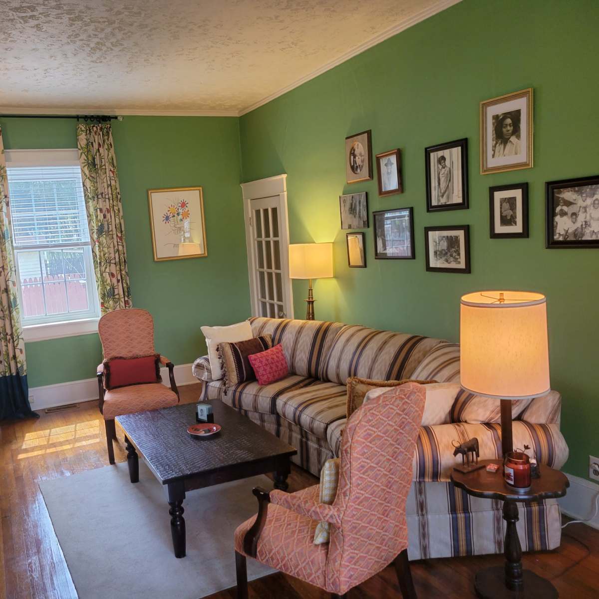 The living room features a green wall, a striped sofa, two armchairs, a coffee table, and various framed pictures hanging on the walls.