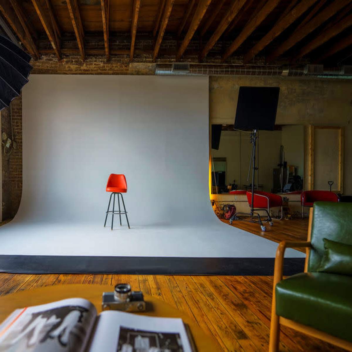 A photography studio featuring a red chair positioned on a white backdrop, surrounded by lights and a large window.
