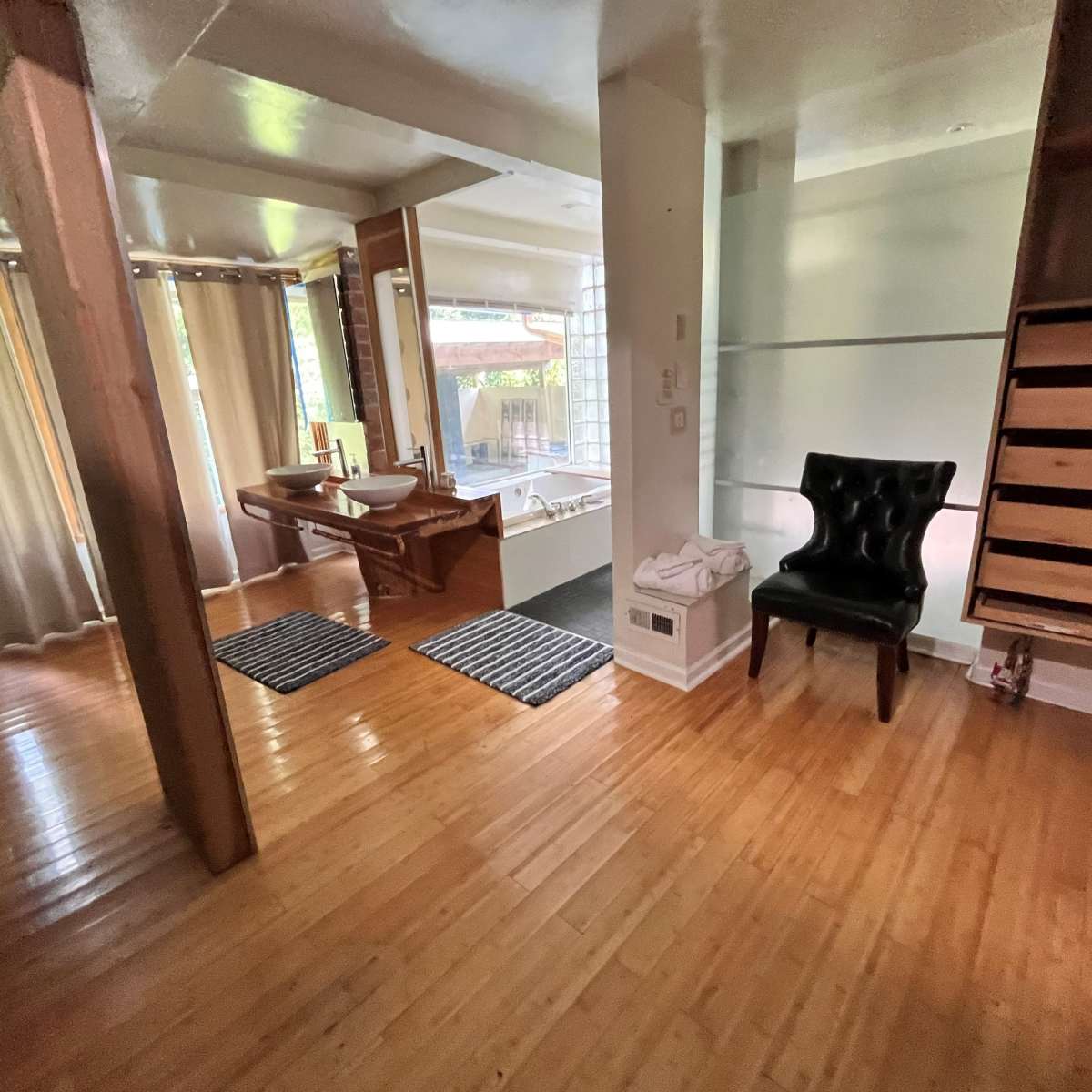 A well-lit open space featuring a wooden floor, a chair, a vanity area with a sink, and a view into a bathroom area with a tub.