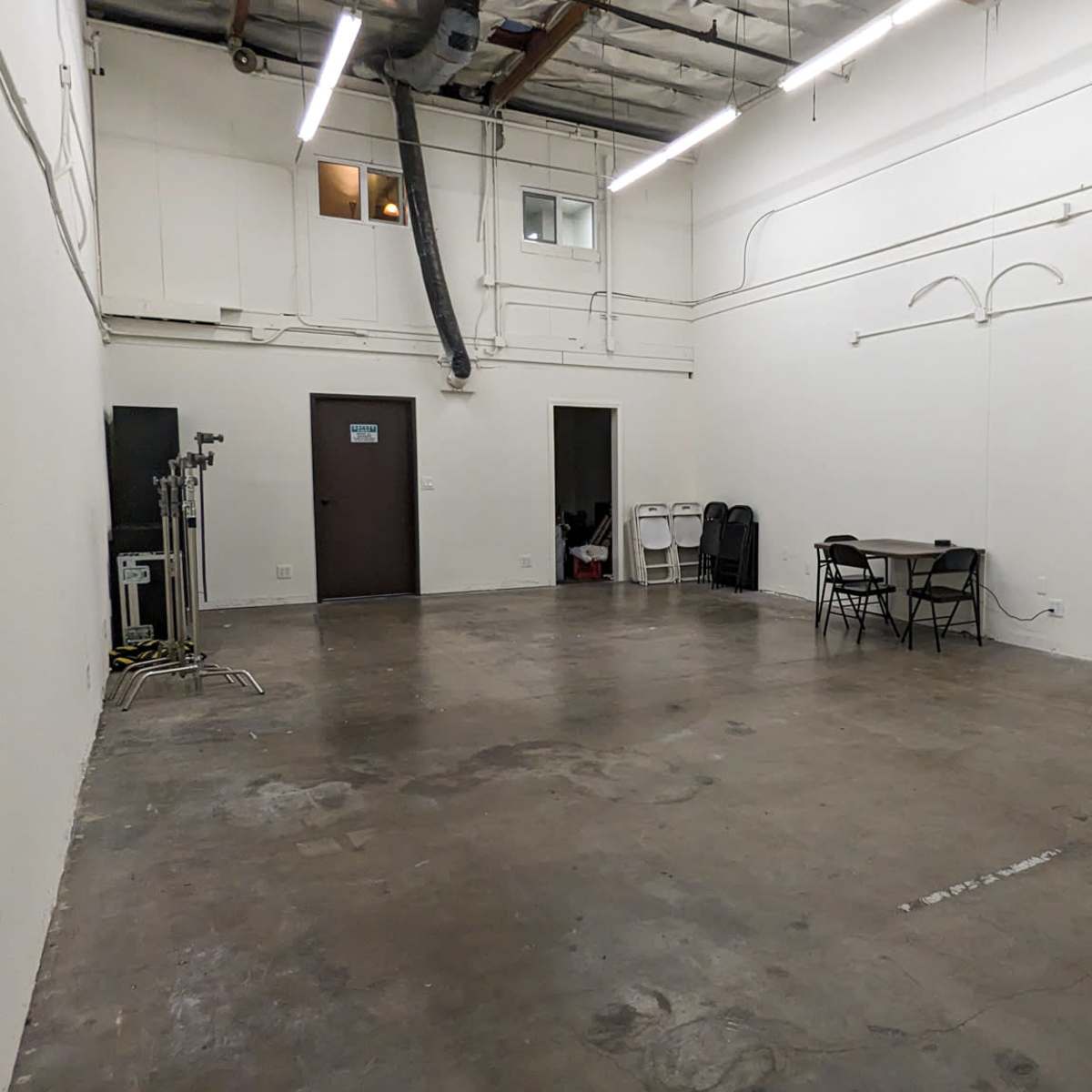 A spacious, empty indoor area with concrete flooring, white walls, and a few folding chairs and tables.