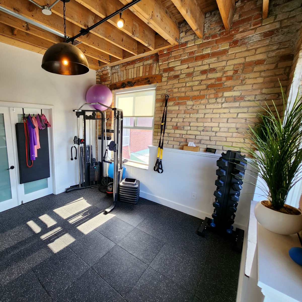 A well-equipped home gym featuring exercise equipment, weights, and fitness accessories in a room with exposed brick walls and wooden beams.