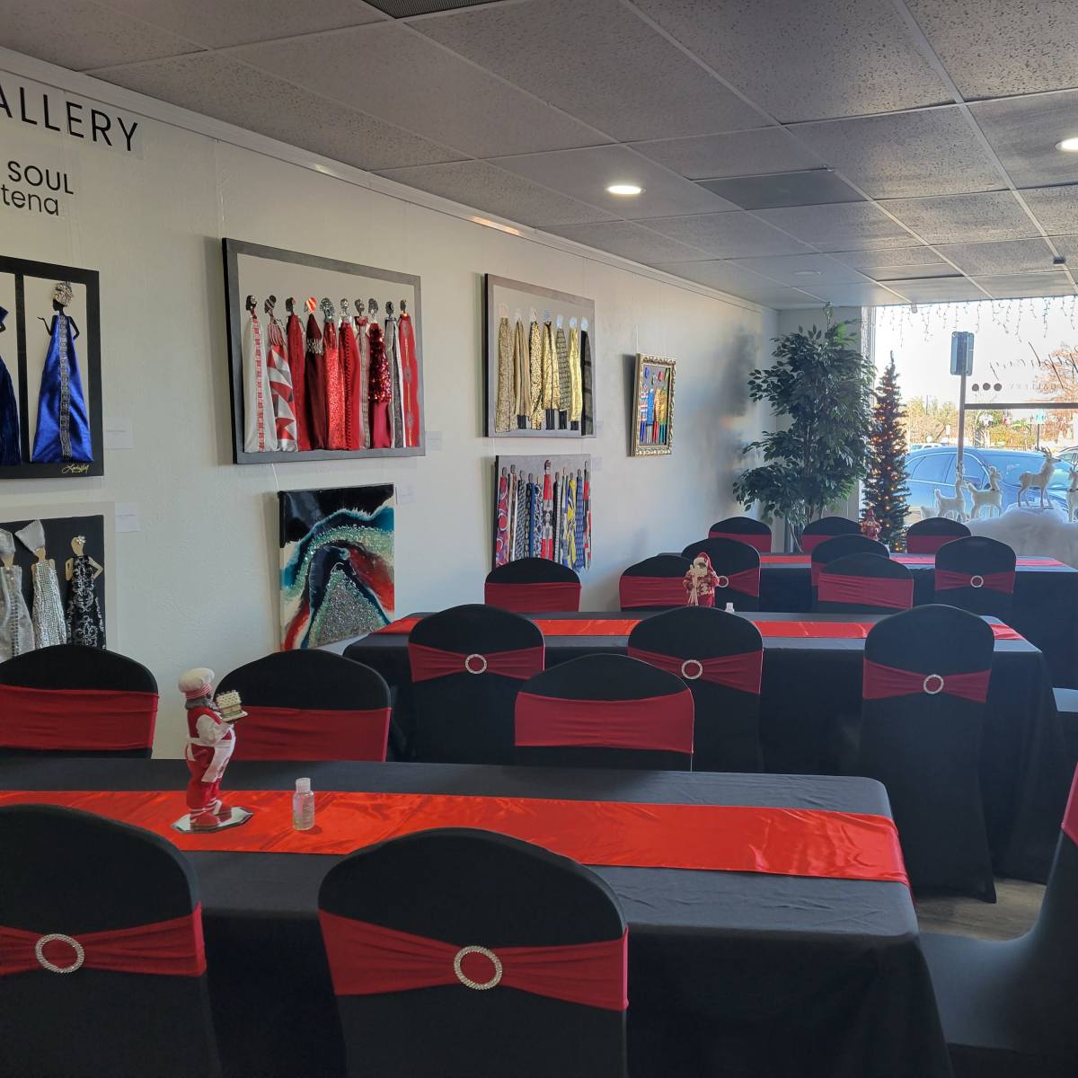 The interior of an art gallery features tables adorned with black and red tablecloths, surrounded by decorated walls displaying various artworks and trees in the background.