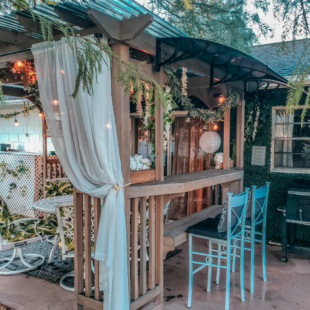 A cozy outdoor seating area with wooden furniture, decorative plants, and soft lighting.