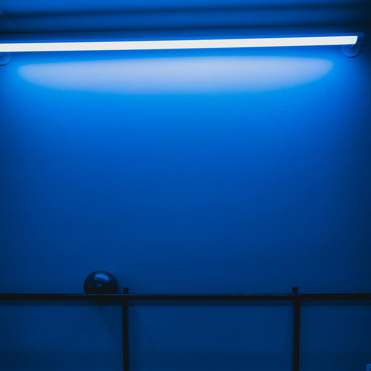 A black sphere sits on a railing beneath a blue-lit wall.