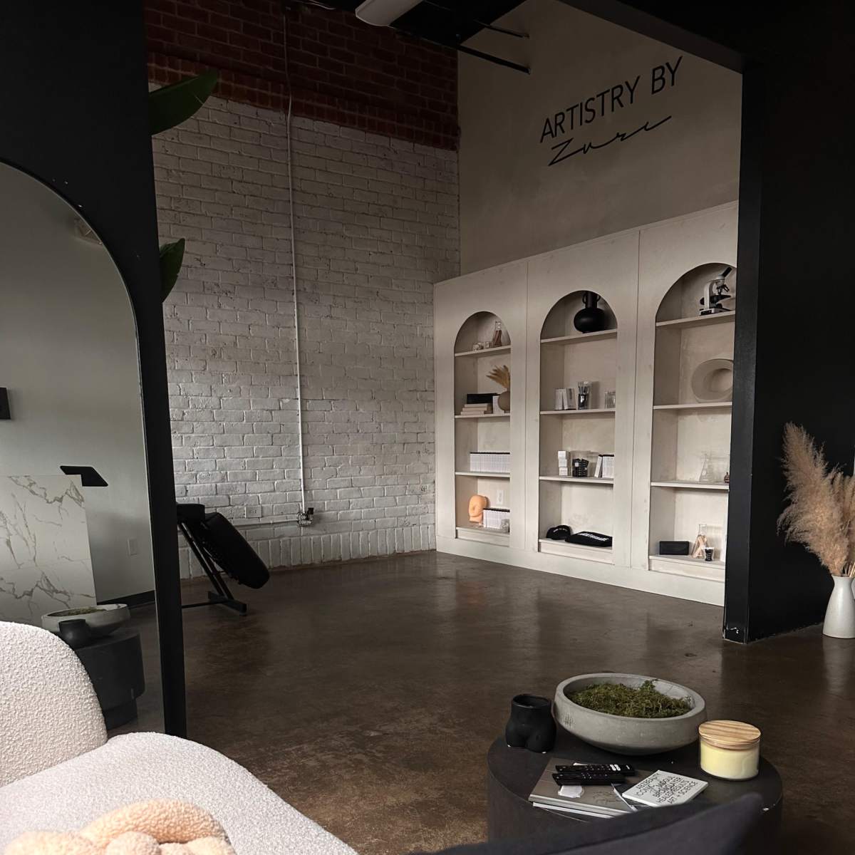 A modern interior space with a minimalistic design featuring a cozy seating area and a display shelf with various decorative items.