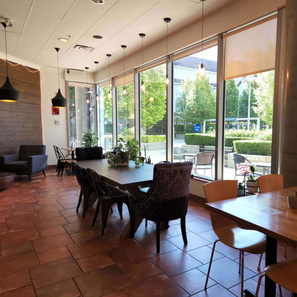 A modern café interior with large windows, natural light, and a mix of seating arrangements, including wooden and upholstered chairs.