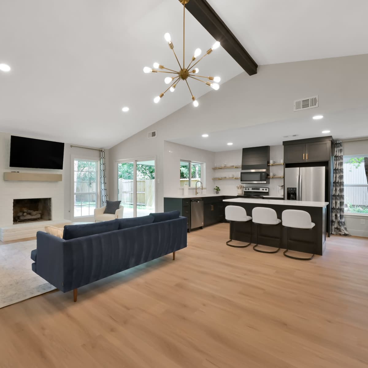 A spacious living area with a fireplace, modern kitchen, and seating arrangements, featuring large windows that provide natural light.