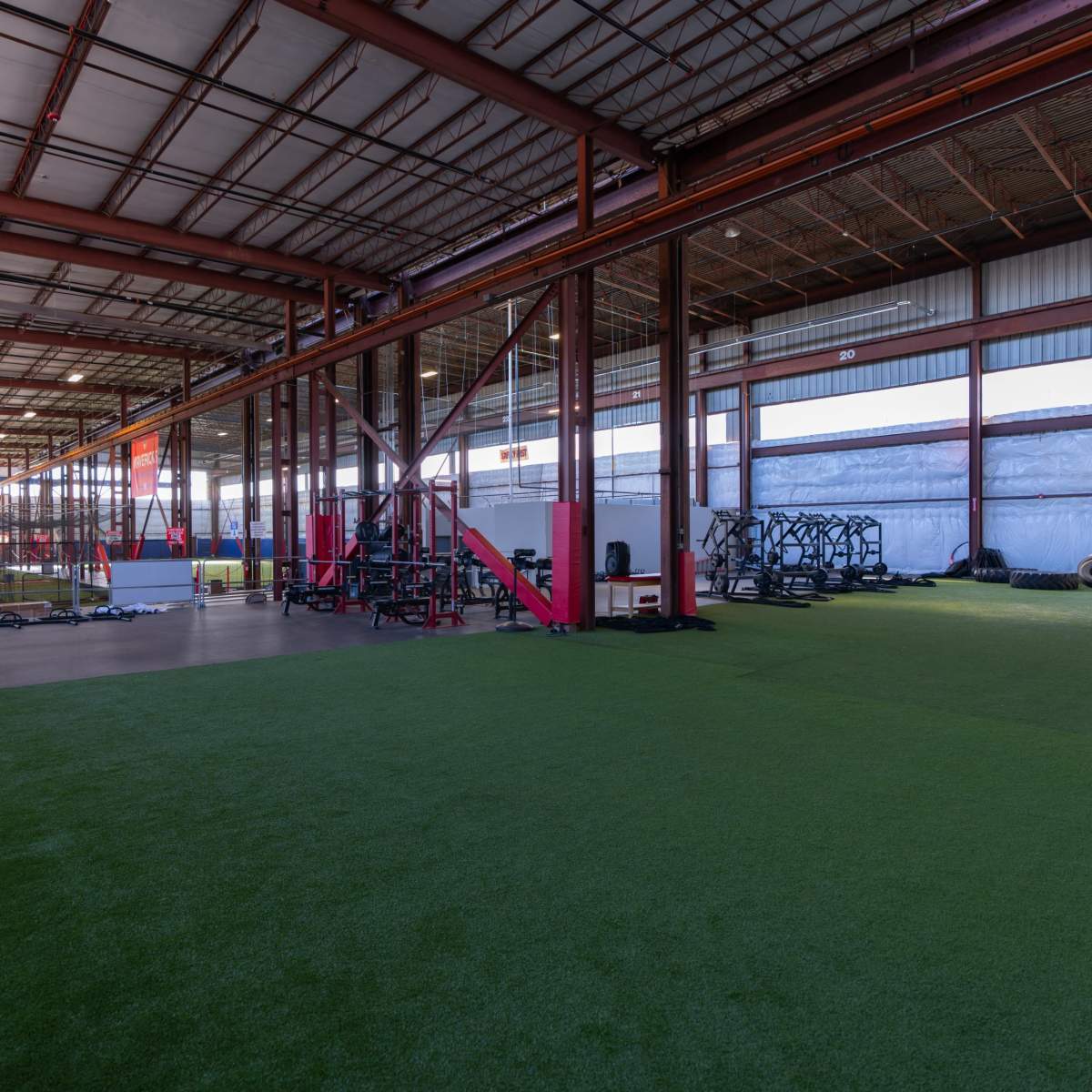 A spacious indoor training facility with artificial grass flooring and various exercise equipment arranged along the walls.