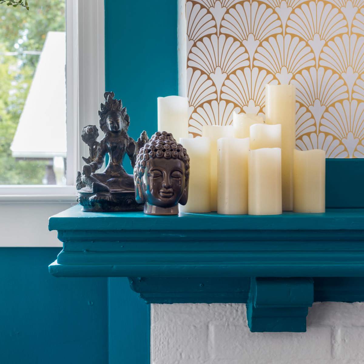 A wooden shelf features decorative items, including a Buddha statue, a small figure of a deity, and several LED candles against a teal wall.