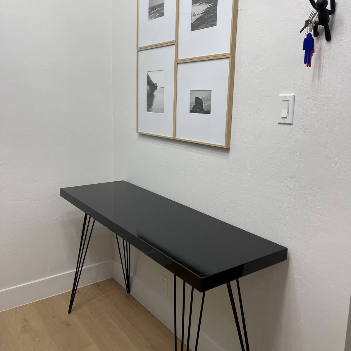 A black table with slender legs is placed against a white wall, adorned with four framed black-and-white photographs above it.