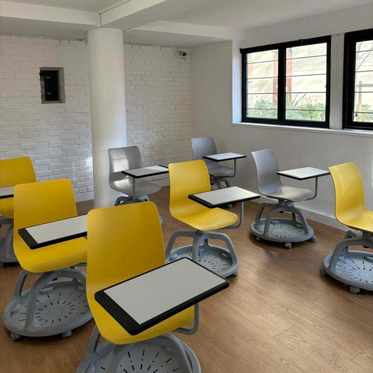 A modern classroom with yellow and gray chairs arranged around small tables, set against a bright, minimalist interior.