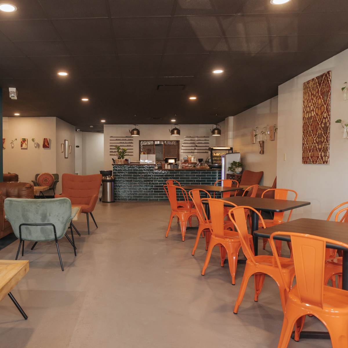 A café interior featuring orange chairs, a wooden table, and a green wall with neon signage, along with a service counter in the background.