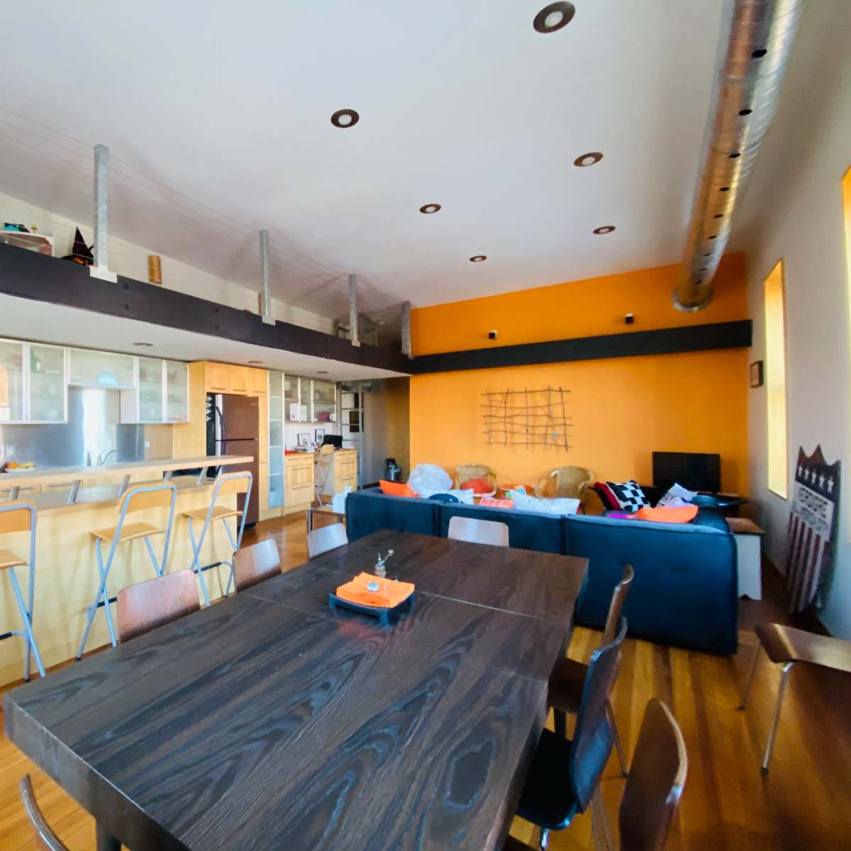 A modern kitchen and dining area with a wooden dining table, bar seating, and an orange accent wall.