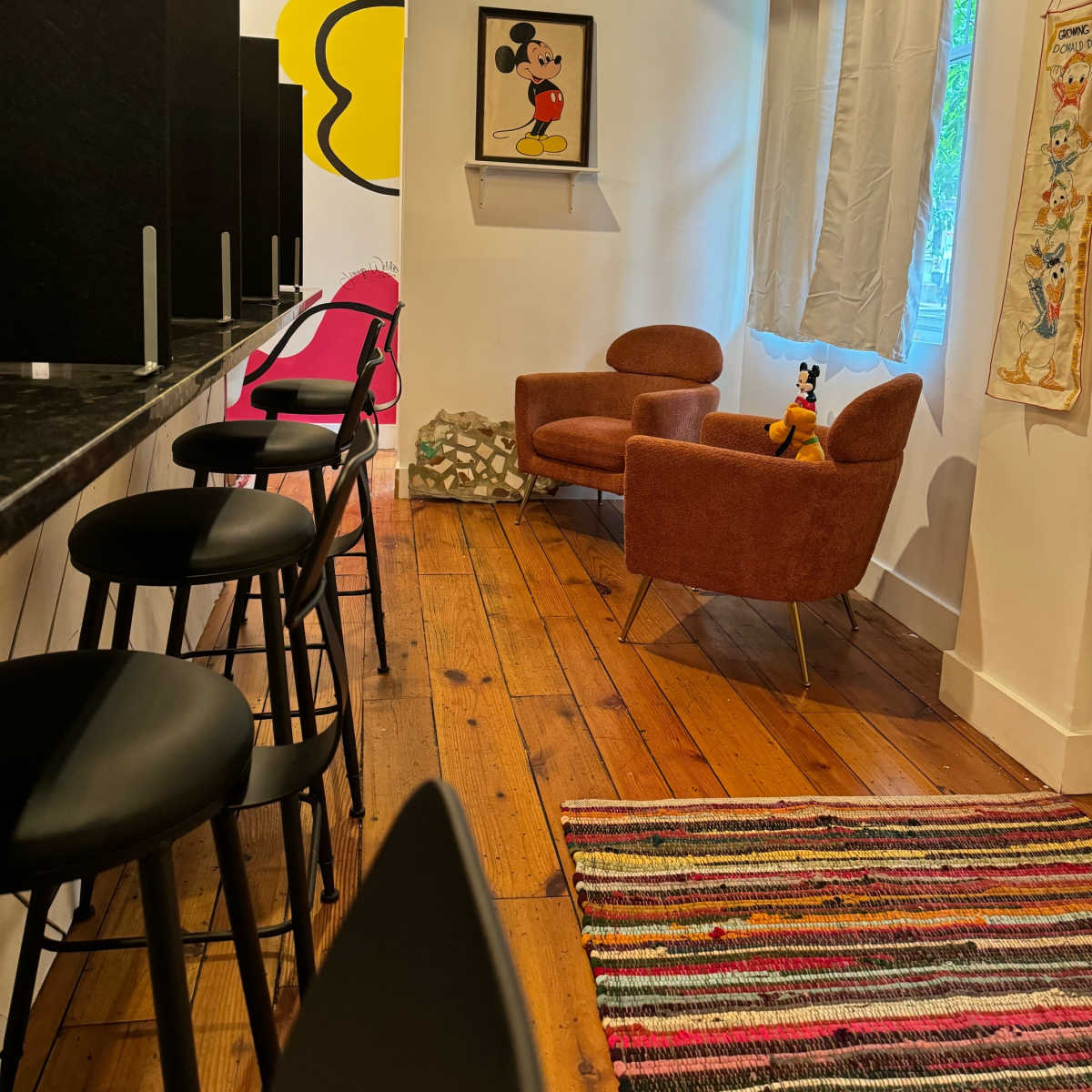 A cozy indoor space featuring a pair of orange armchairs, a colorful rug, and a wall adorned with a framed cartoon artwork of a character.