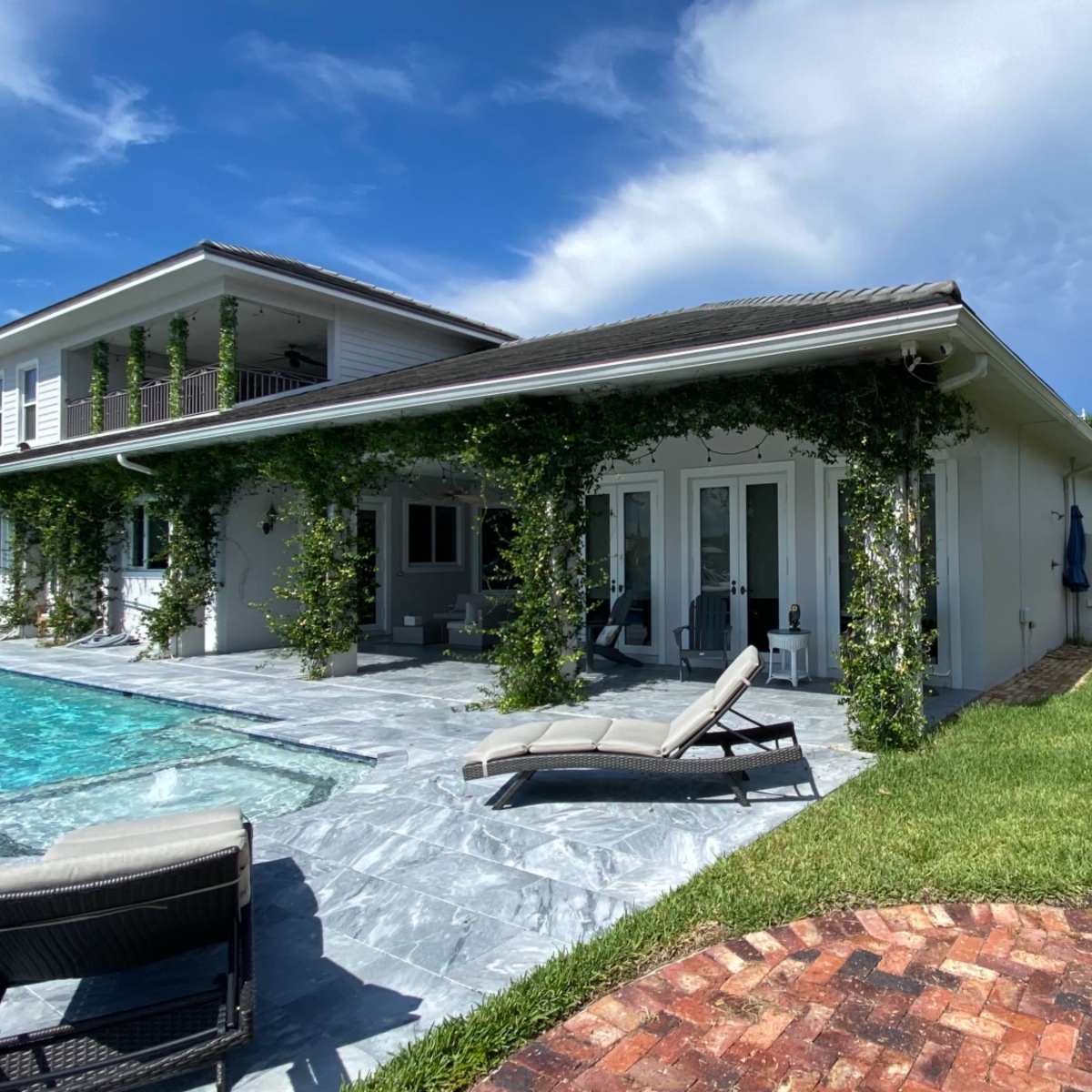 A modern two-story house with a swimming pool and lounge chairs is surrounded by greenery and a well-maintained lawn.