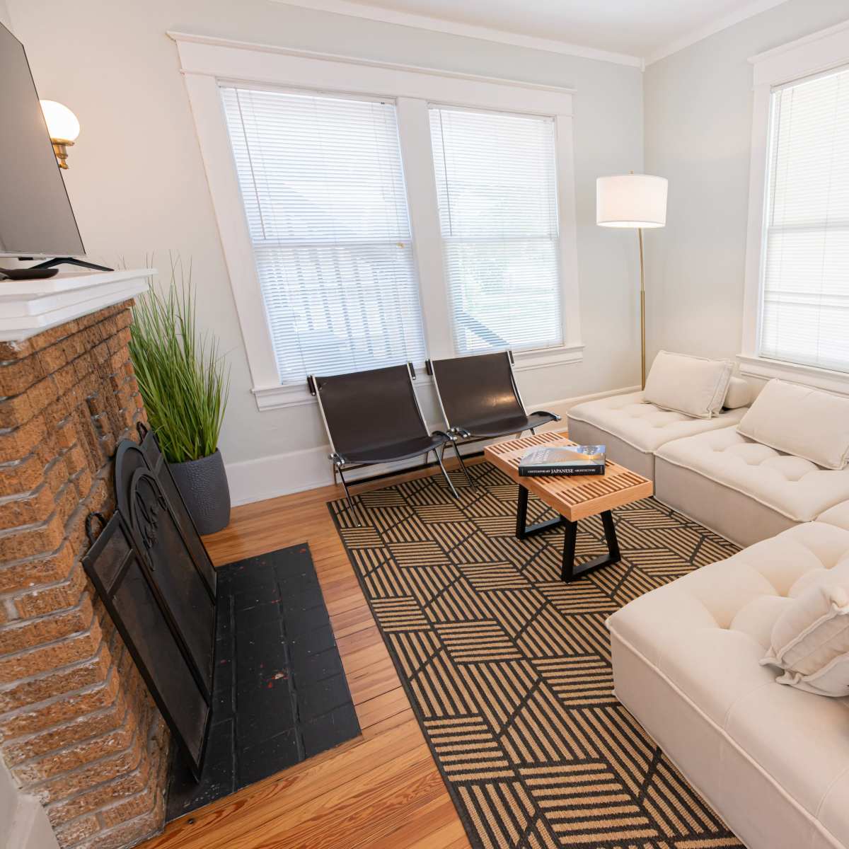The living room features a sectional sofa, a coffee table, and large windows that provide natural light.