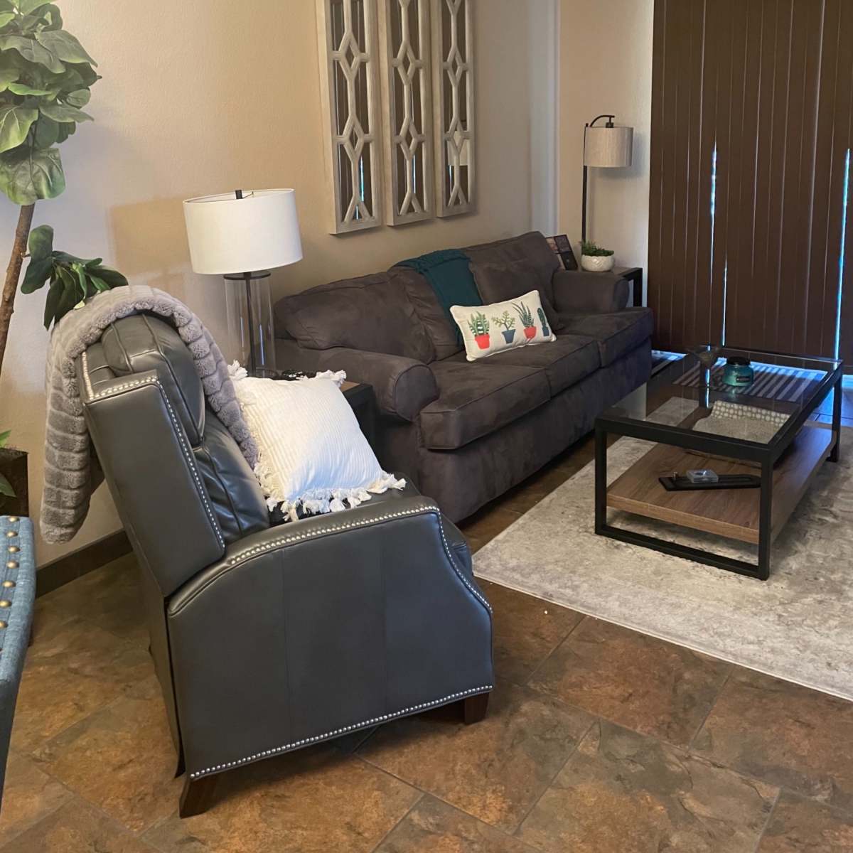 A living room with a gray sofa, a matching chair, a glass coffee table, and decorative wall art.