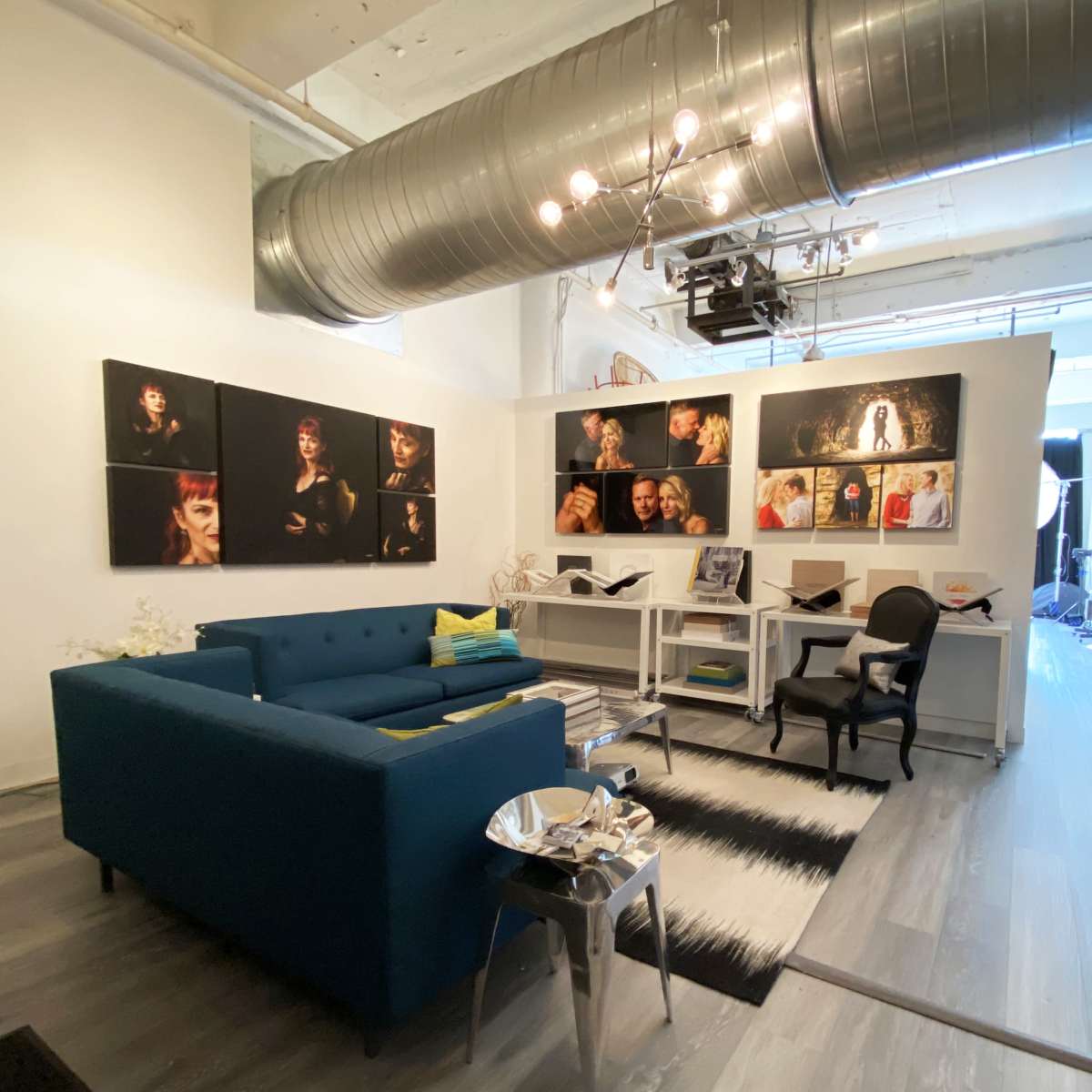 A modern studio space featuring a blue couch, white desks with chairs, and several framed photographs displayed on the walls.
